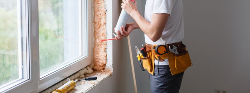 person using spray insulation to fill air gaps around window